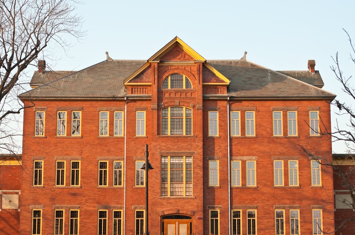 Three-story red brick Victorian mansion with symmetrical windows and peaked roof representing historic Old Main