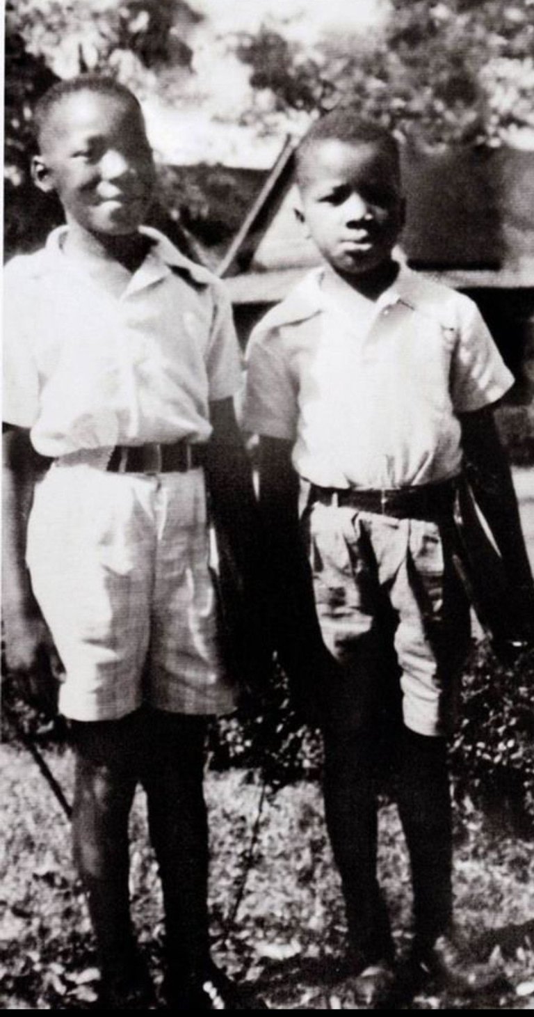 Black and white photograph of two young men in uniforms standing outdoors with trees in background