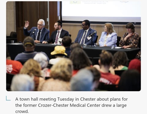 Panel of officials at a town hall meeting with a large audience seated in foreground discussing Crozer-Chester Medical Center plans